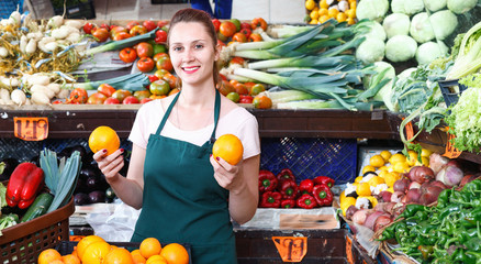 Obraz premium Seller female is holding oranges on her workplace in the market.