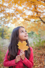 Beautiful girl with yellow leaf in autumn park