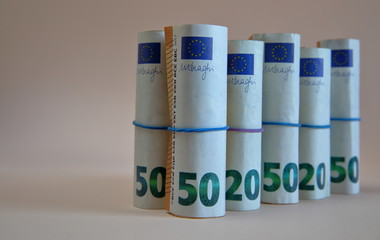 50, 20 and 10 euro banknotes in rolls, tied with elsctic blue and violet thin rubbers close up isolated, copy space on left side