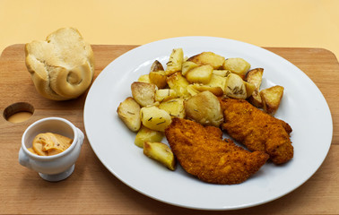 Fried chicken with roasted potatoes, bread and sauce, on wooden table