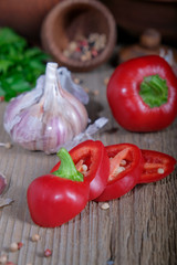 Red bell pepper, garlic, greens, spices on a wooden table.