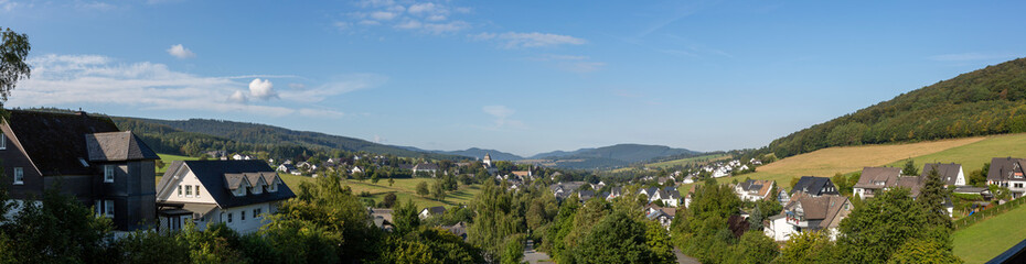 Fototapeta na wymiar Wide panorama of a valley in Sauerland, Germany, with the spa village of Graftschaft and the pilgrimage Wilzenberg mountain at sunrise