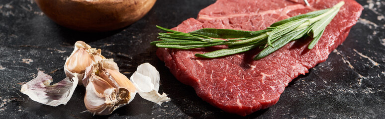 panoramic shot of uncooked beef sirloin with rosemary sprig near garlic on black marble surface