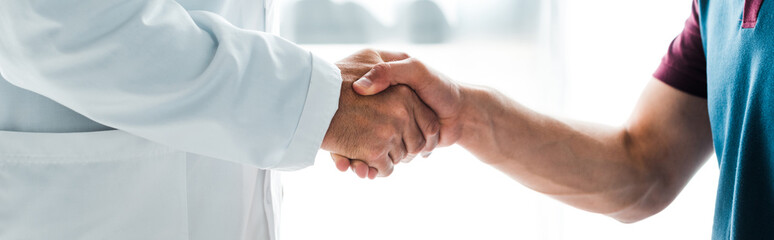 panoramic shot of doctor in white coat shaking hands with man