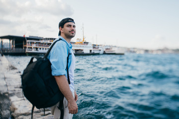 Portrait of a young man against the background of the sea, city, pier and ships.