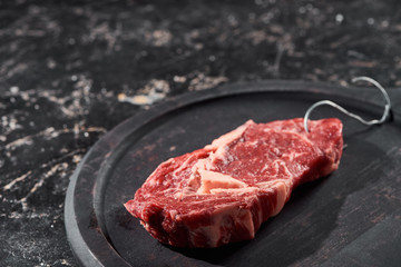 raw meat with hook on wooden plate on black marble surface