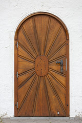 Detail of a wooden church door with symbol of the sun in a white plaster wall