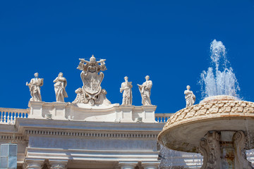 Fototapeta na wymiar Fountain and detail of the Chigi coats of arms and the statues of saints that crown the colonnades of St. Peter Square built on 1667 on the Vatican City