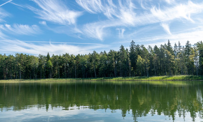 Fototapeta na wymiar Lake shines green in summer under blowing clouds, white clouds of interesting shape reflect on lake surface, Lake Valdis, Turna, Latvia