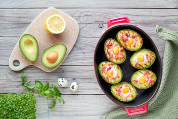 Top view on grilled avocado boats with bacon and quail eggs, flat lay on wood