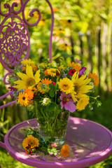 Colorful summer flower bouquet in a vase on a pink garden chair