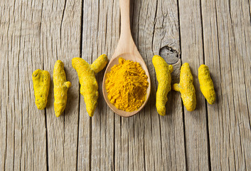 Turmeric peeled root and turmeric powder in wooden spoon on wooden rustic background, healthy spice curcumin ( curcuma longa )