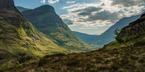 View of valley in Glencoe Scotland in morning with shadows and road snaking through to lake in...