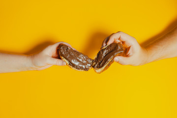 hands holding bread slices spread with chocolate on a yellow background