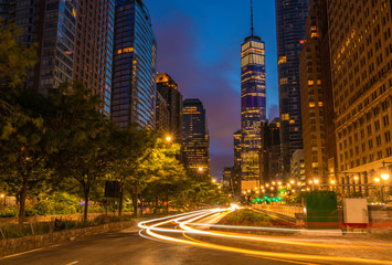 Downtown Manhattan street view at dawn featuring car lights on the foreground and buildings on the...