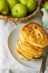 Stack of homemade mascarpone pancakes fritters on plate on white cotton tablecloth pears in wicker basket. Breakfast setting cozy homely atmosphere