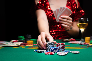 A girl in an evening red dress plays with cards in a casino raising the stacks with croupier chips. Gaming business casinos, night clubs