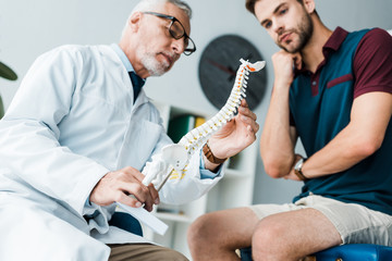low angle view of bearded doctor holding spine model near patient in hospital