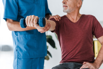 cropped view of doctor standing near middle aged patient exercising with dumbbell