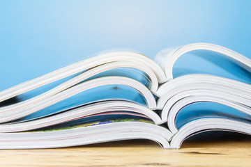 pile of magazine on wooden table over blue background with copy space