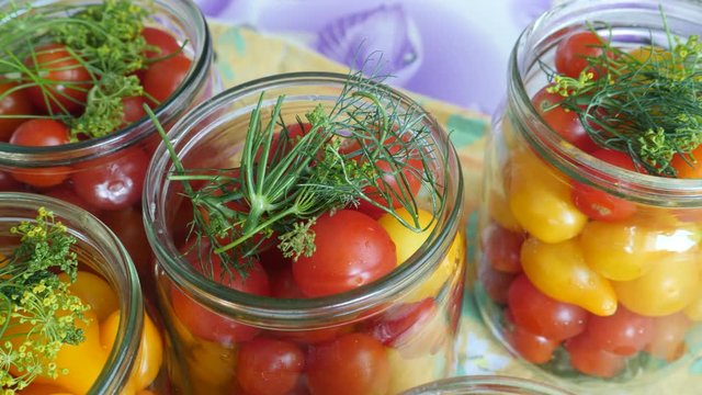 Housewife puts dill in a glass jar with tomatoes. Homemade pickled canned red and uellow tomato with herbs. Home preservation