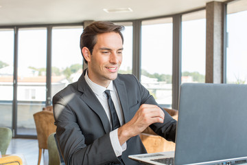 Handsome young businessman working on his notebook in hotel cafe