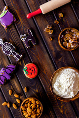 Cooking halloween cookies in shape of spooky figures, rollin pin, nuts and flour on wooden background top view