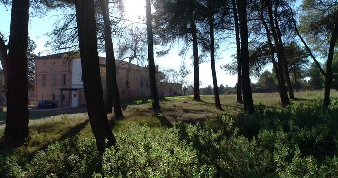dron vuela cerca del suelo esquivando los &aacute;rboles de bosque mediterr&aacute;neo acercandose a ermita abandonada