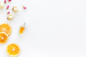 Feminine desk with perfume bottle, flowers and dry oranges on white background top view copy space