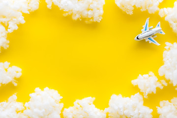 Fly by plane concept. Airplane model and clouds on yellow background top view frame copy space