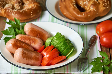 Fried sausages and slices of fresh vegetables on a white plate 