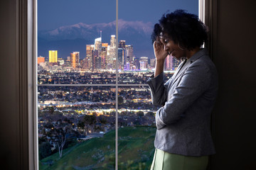 Black female businesswoman looking worried or tired by an office window with a view of downtown Los...