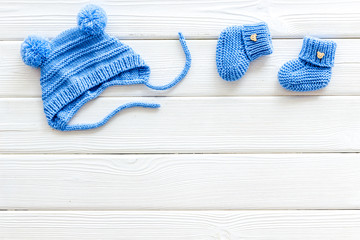 Knitted blue footwear and hat for baby on white wooden background top view mockup
