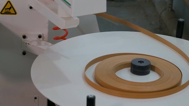 Machine for edging chipboard parts. Movement of a roll of brown edge for gluing on furniture details. The real sound of a working woodworking machine.