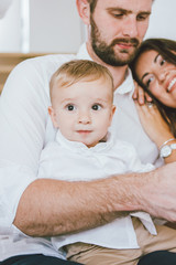 Obraz premium Cute baby boy in white shirt with his happy family in bright interior, close up portrait