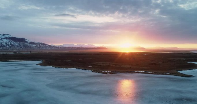 Flying Fantom 4 pro Drone in Iceland shoting frozen lake at sunrise near the mountains
