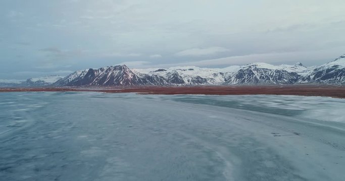Flying Fantom 4 pro Drone in Iceland shoting frozen lake at sunrise near the mountains