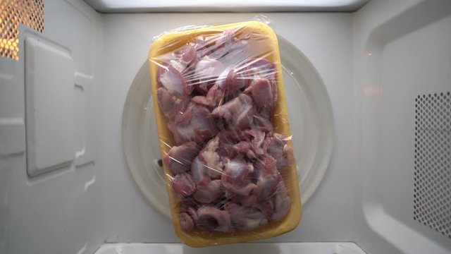 Fresh raw сhicken offal in food tray with plastic wrap rotating in microwave top view.