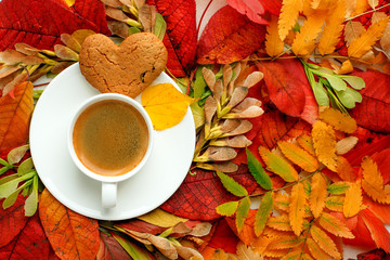 Autumn, fall leaves, hot steaming cup of coffee and a warm on table background. Seasonal, morning coffee, Sunday relaxing and still life. Bright cafe menu concept