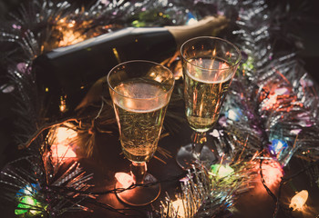 Two Glasses with champagne and bottle on a wooden table decorated with Christmas accessories to celebrate the new year and Christmas. Romantic evening. The glow from the garlands