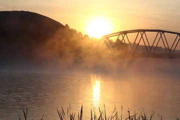 Fototapeta na wymiar sunrise on the background of the bridge over the misty river