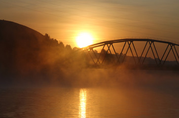 Fototapeta na wymiar sunrise on the background of the bridge over the misty river