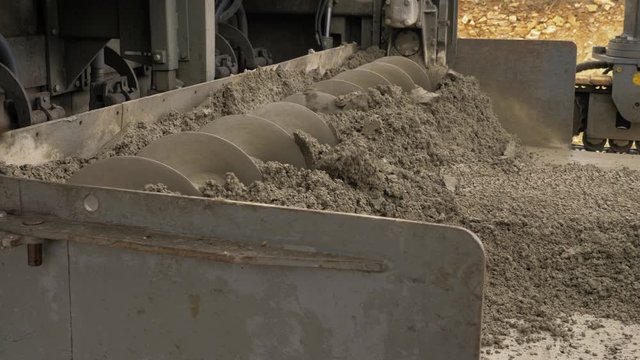 Fully mechanised process of concrete pavement construction. The slipform paver spreads the concrete over the full paving width with its auger. Preparation for laying a base layer. Shot left to right.