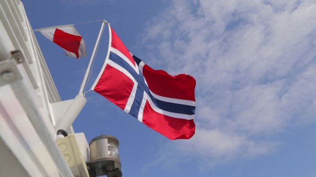 Sunlit Norwegian flag on boat waving in wind against blue sky