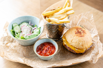 Cheeseburger with lettuce, tomato, fries, and melted cheese. The table in the restaurant. Unhealthy food.