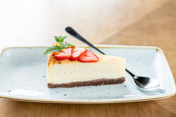 Piece of delicious cheesecake with strawberry and mint leaves on white plate.