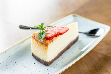 Piece of delicious cheesecake with strawberry and mint leaves on white plate.