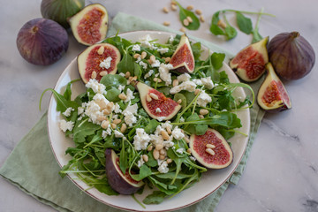 Fig salad with feta cheese, nuts and arugula on wooden background