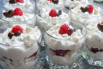 Fresh cream desserts in glasses with crumbles, a chocolate heart and one raspberry
