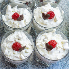 Fresh cream desserts in glasses with crumbles, a chocolate heart and one raspberry, square